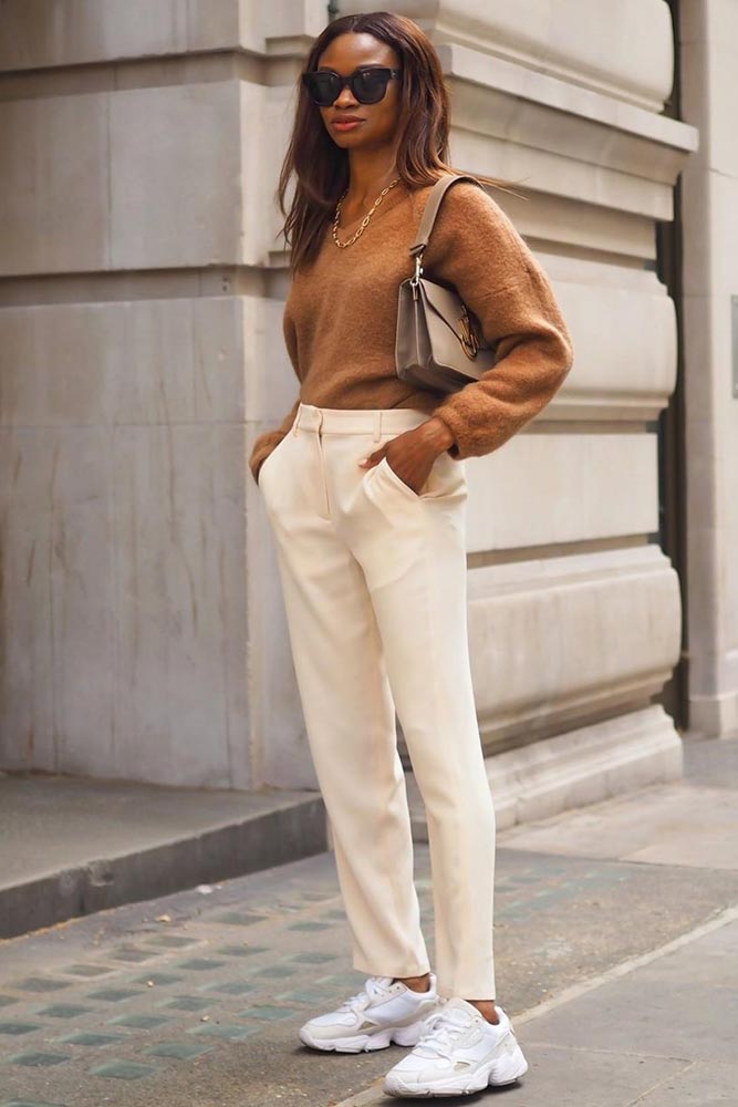 Premium AI Image | A woman in a grey sweater and white pants stands in an  alley wearing a hat and sunglasses.