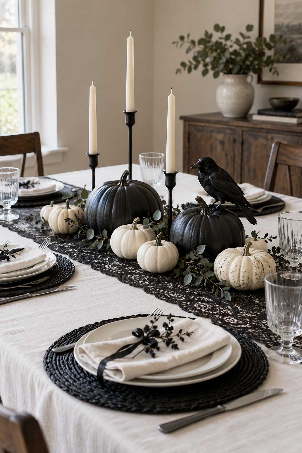 Elegant Halloween table with black and white pumpkins, ivory taper candles, a black lace runner, and a decorative raven